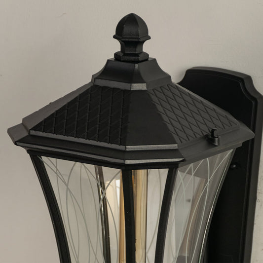 Close view of the black wall lantern highlighting its detailed metal frame clear patterned glass panels and glowing bulb.