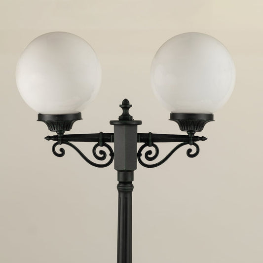 Closeup view of the double-globe lamp post showing the ornate metal detailing near the top of the pole and the smooth frosted finish of the round globes.